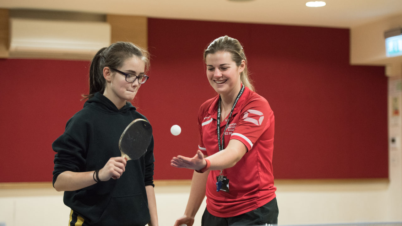 PGCE student with pupil teaching table tennis