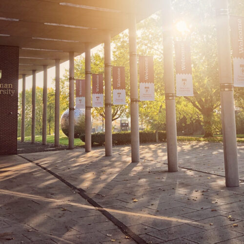 Newman front of campus with welcome flags and sun shining