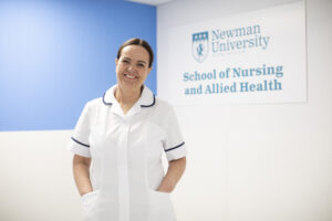 A trainee nurse at Newman standing in front of Applied Nursing signage