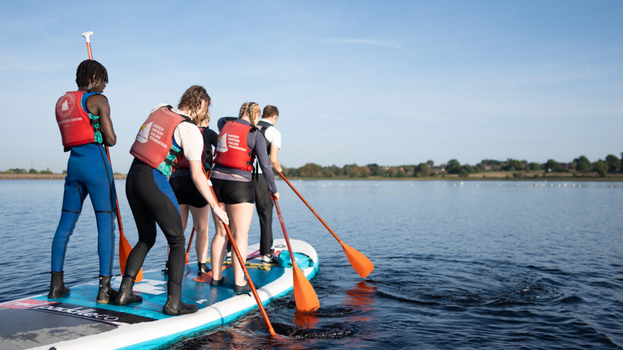 Students standing on paddleboard on reservoir