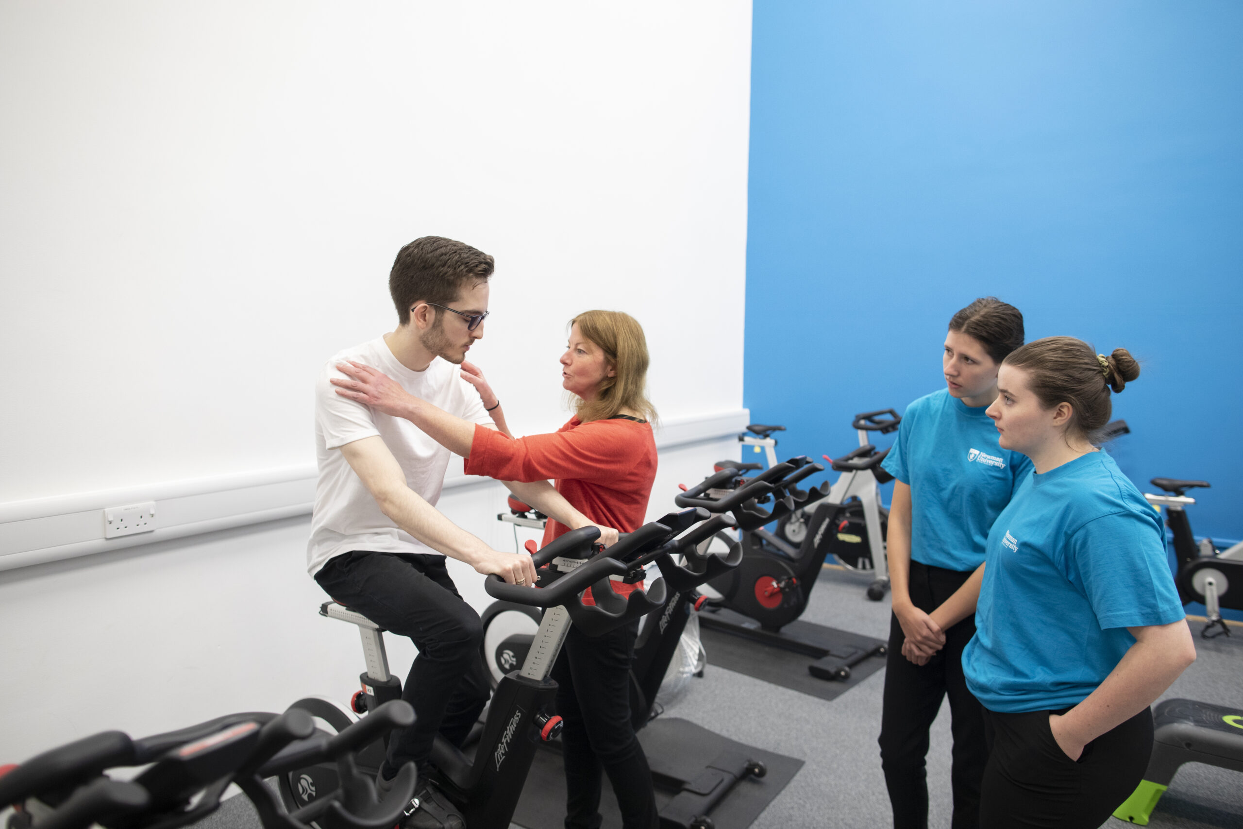 Physiotherapy lecturer talking to student on exercise bike with two students watching