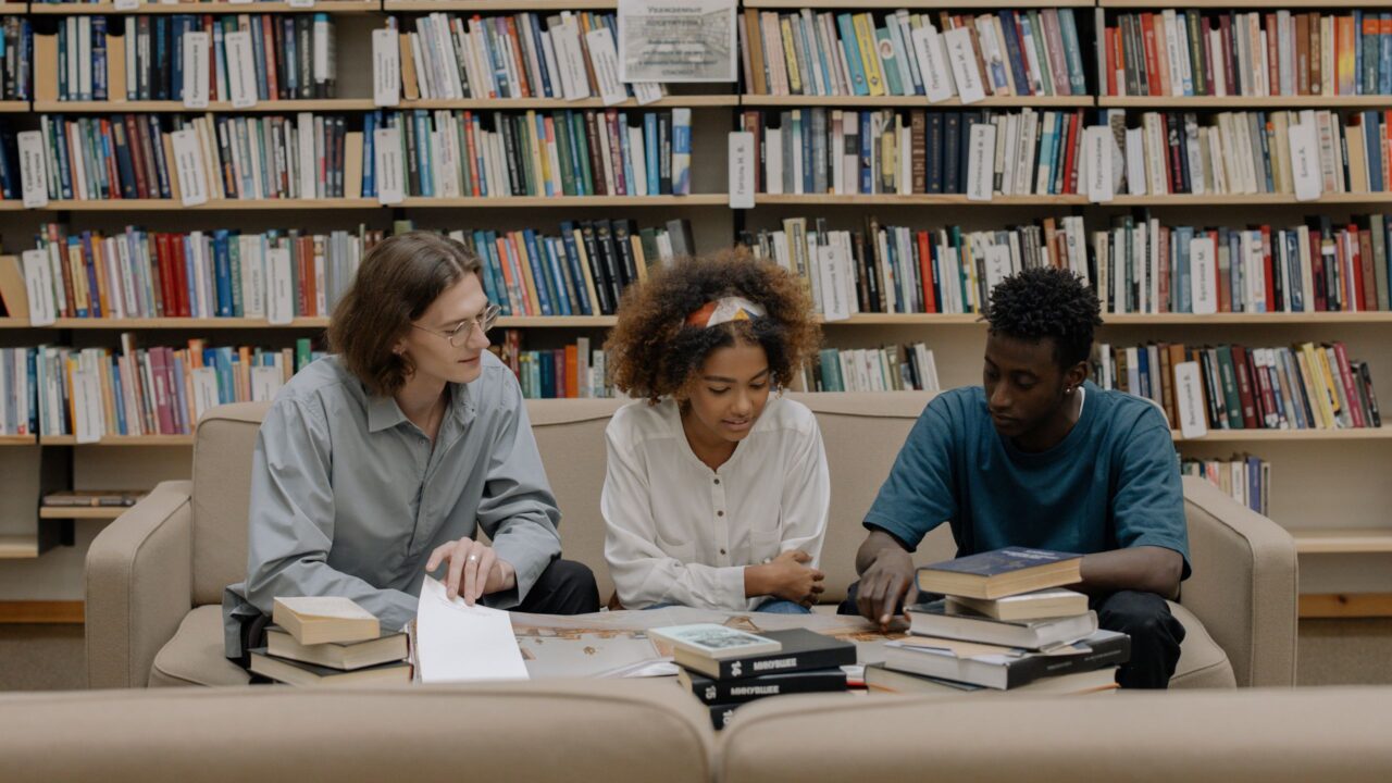 Students sitting down in a library looking at books together.