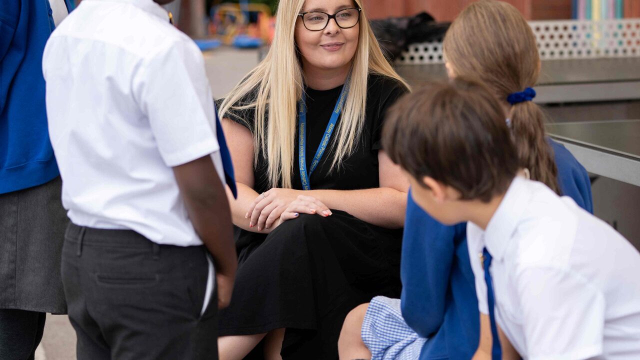 Teacher sat in playground with group of primary school pupils