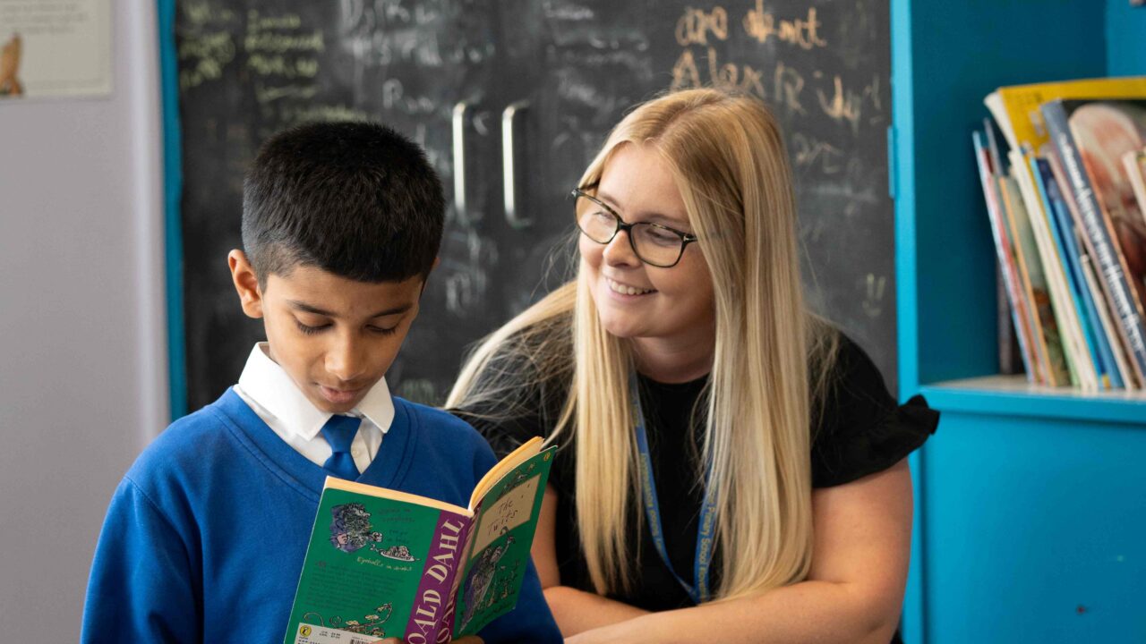 Primary school child reading to teacher in corner of classroom