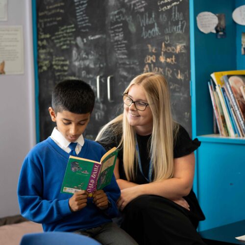 Primary school child reading to teacher in corner of classroom