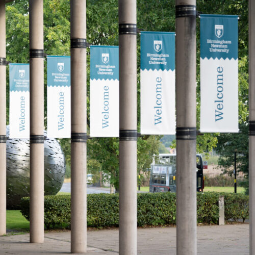 Welcome banners on pillars hanging outside Birmingham Newman University's campus