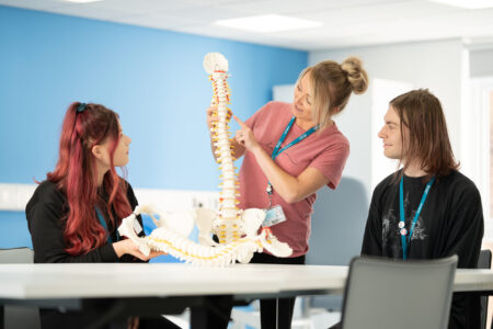 Physio teacher with students looking at back bone skeleton