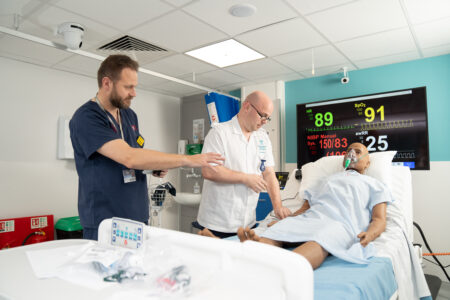 Nursing lecturer is giving student nurse guidance on treating a patient in a simulation ward.