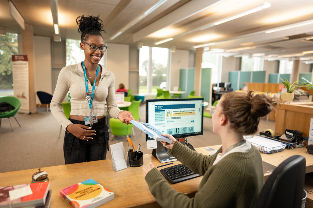 Student in the Birmingham Newman University Library, receiving advice from a member of staff.