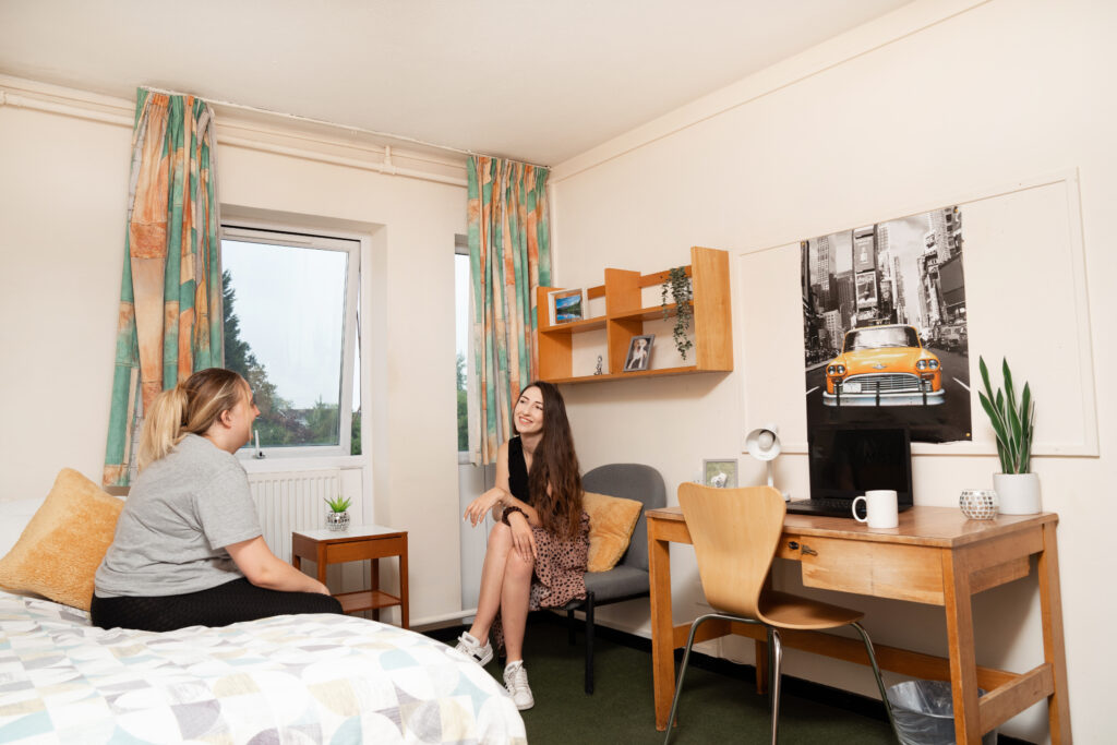 Two students talking in halls of accommodation bedroom.