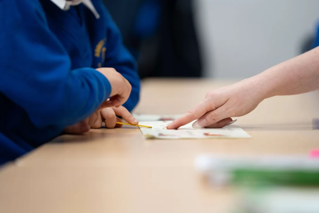Teachers hand pointing at piece of paper in class